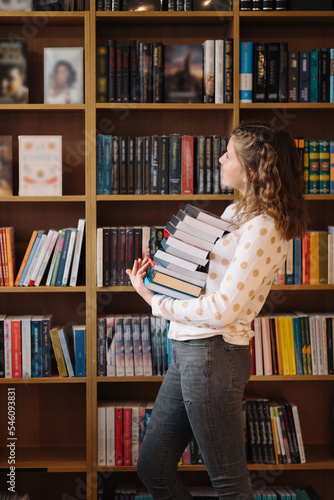 Teen girl among a pile of books. A young girl holding books with shelves in the background. She is surrounded by stacks of books. Book day.