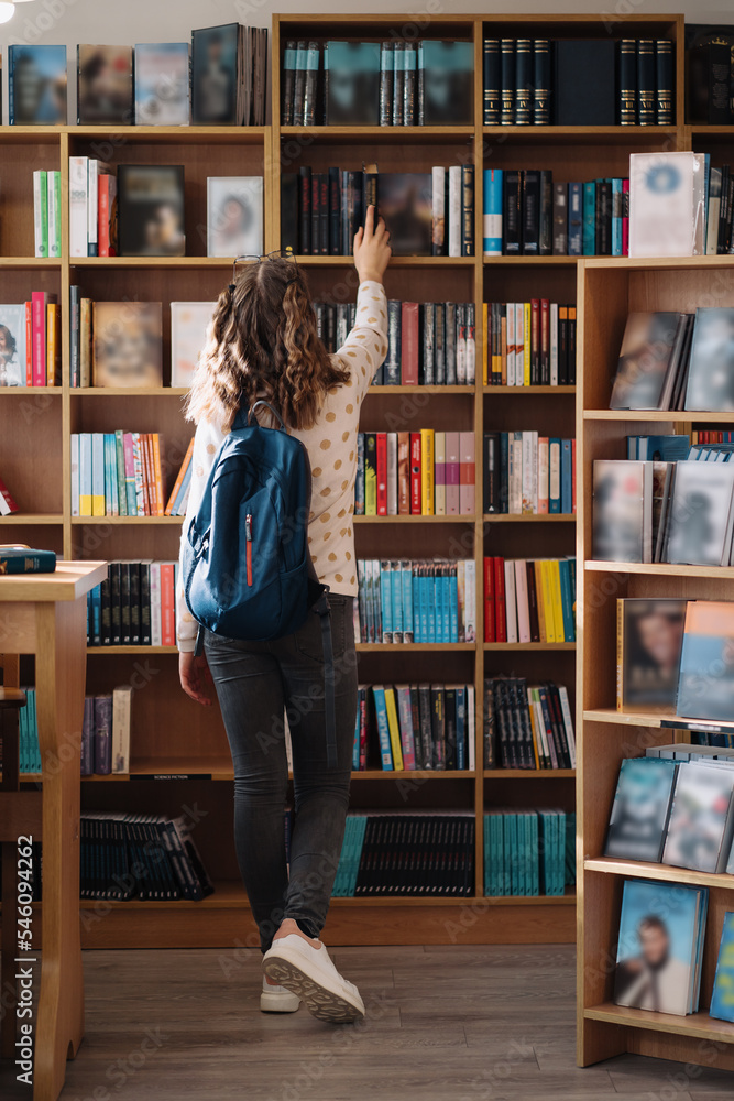 Teen girl among a pile of books. A young girl holding books with shelves in the background. She is surrounded by stacks of books. Book day. Teen girl among a pile of books. A young girl holding books with shelves in the background. She is surrounded by stacks of books. Book day.