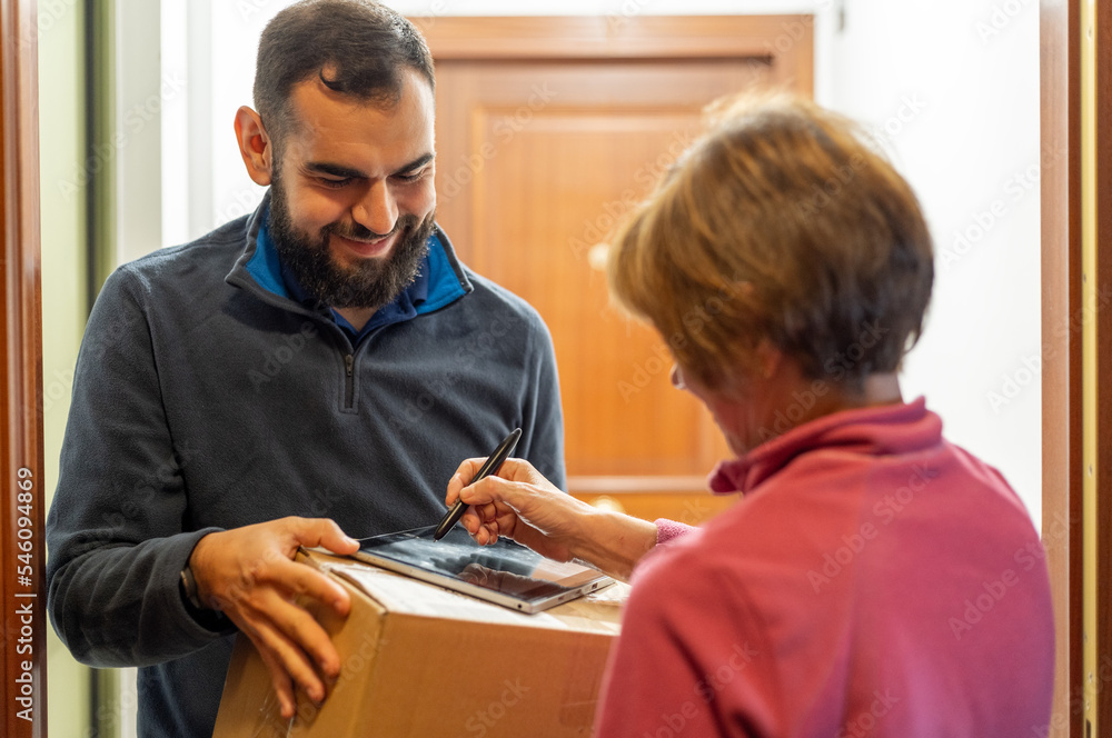 Bearded man delivering a package to a lady. Holding a parcel in front of the door. Signing on a tablet