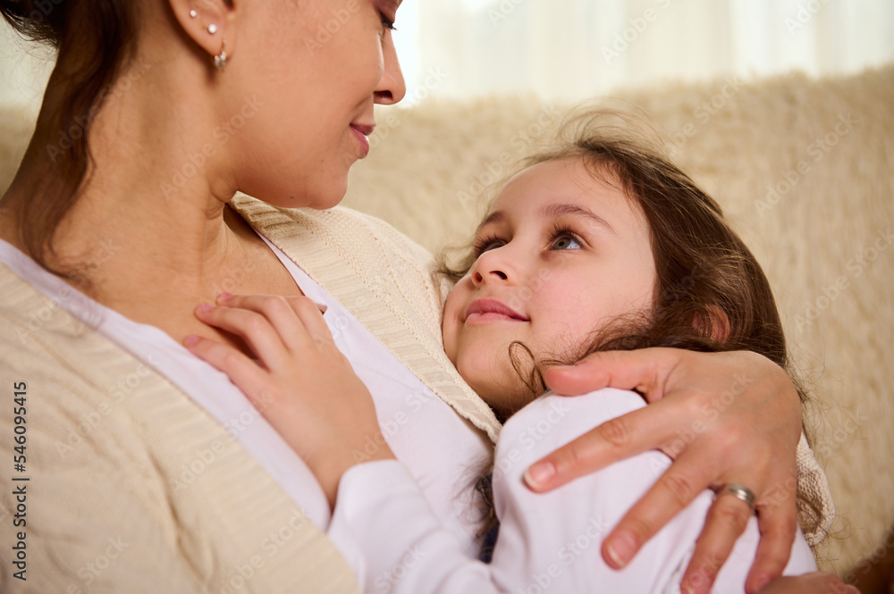 Selective focus on a beautiful little girl falling asleep in the arms of her loving mother, who admires her, feels a sense of love, care and gratitude. Carefree childhood. Happy family. Children's Day