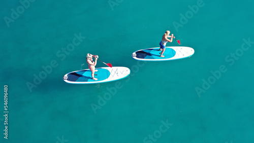Aerial drone photo of two women practising Stand Up Paddle board or SUP surf in tropical exotic island bay with emerald crystal clear sea photo