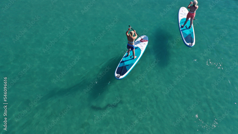 Aerial drone photo of two women practising Stand Up Paddle board or SUP surf in tropical exotic island bay with emerald crystal clear sea