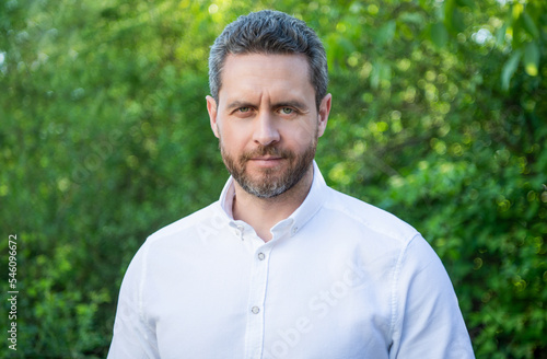 Portrait of handsome man with unshaven face in white shirt natural background