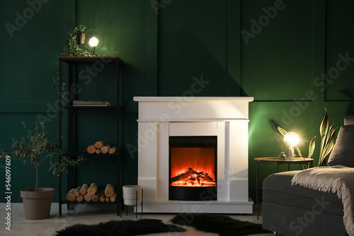 Interior of dark living room with fireplace, glowing lamps and shelving unit © Pixel-Shot