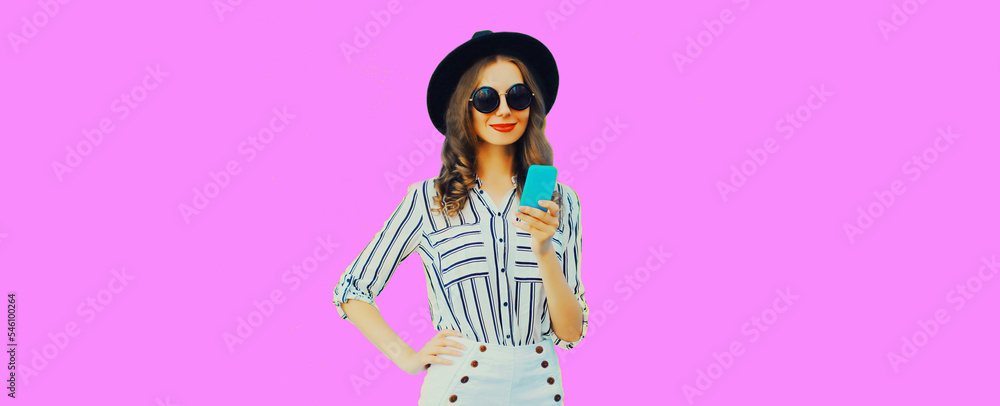 Portrait of stylish happy smiling young woman model with smartphone wearing black round hat, striped shirt on pink background, blank copy space for advertising text Portrait of stylish happy smiling young woman model with smartphone wearing black round hat, striped shirt on pink background, blank copy space for advertising text