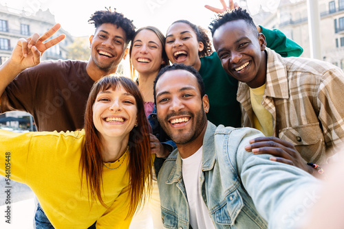 Happy young group of multiracial best friends having fun together outdoors. Millennial diverse people enjoying time together taking selfie portrait in city street