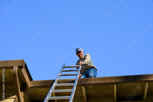 Senior man on apartment building roof ready to climb down an aluminum extension ladder 