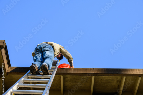 Senior man standing on an aluminum extension ladder cleaning out a roof gutter
