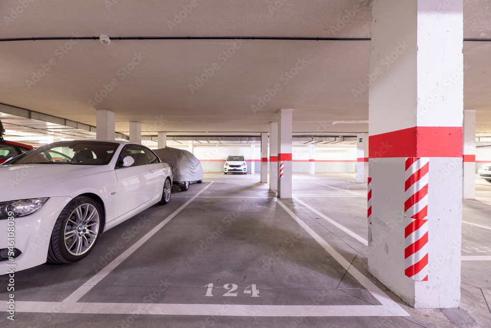 A garage with parked cars, free spaces and columns with warning signs A garage with parked cars, free spaces and columns with warning signs