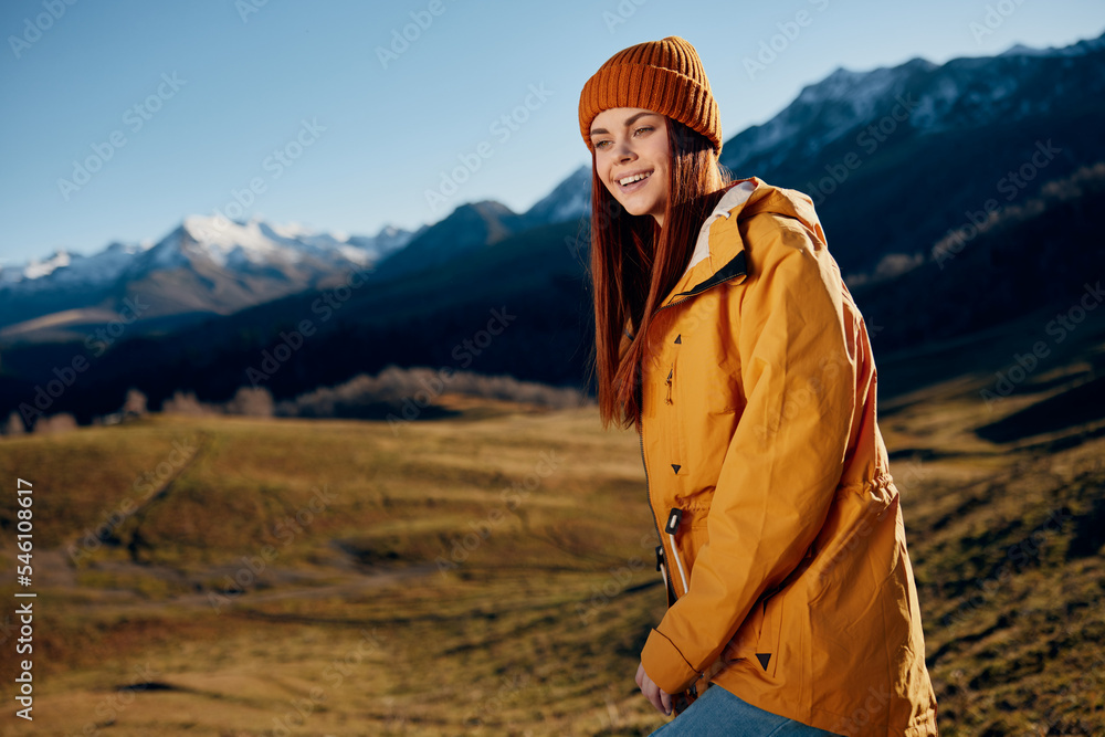 Naklejka premium Woman standing beautifully on a hill smile with teeth in the mountains in the autumn in a yellow raincoat and jeans happy sunset trip to hike the mountains in the snow, freedom lifestyle 