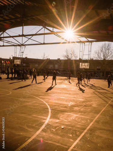 children playing basketball against the light, on a sunny day, with the sun in yellow background