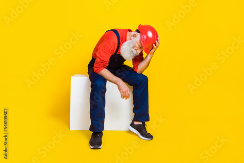 Photo of stressed jobless age man wear overall uniform red hard hat feeling tired isolated yellow color background