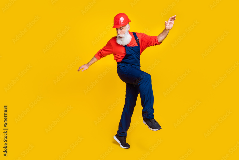 Photo of positive funky age man workwear overall red hard hat dancing having fun isolated yellow color background Photo of positive funky age man workwear overall red hard hat dancing having fun isolated yellow color background