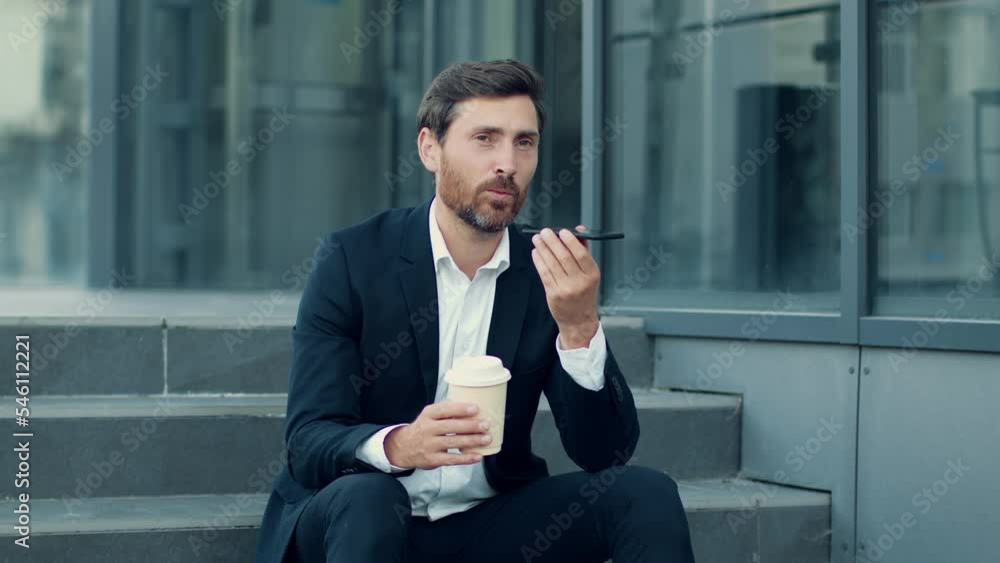 Positive businessman recording audio message on smartphone, enjoying coffee break , tracking shot, free space Positive businessman recording audio message on smartphone, enjoying coffee break , tracking shot, free space