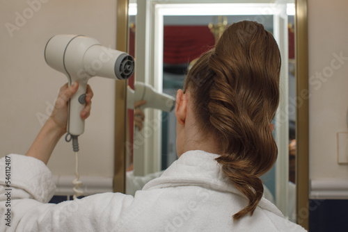 redhead attractive woman drying hair with hair-dryer in bathroom near mirror