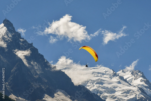 A yellow paraglider flying in front of Mont Blanc mountain in the French Alps in summer, Chamonix-Mont-Blanc, Haute-Savoie, France 