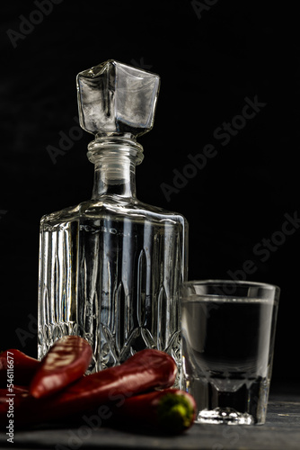 Ukrainian gorilka or vodka or rum or tequila (transparent highly alcoholic drink) in jar and shot. with red pepper on dark background. photo