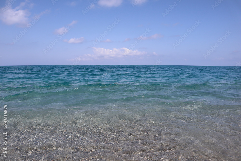 Sea with transparent water and blue sky with clouds on a sunny day, background image