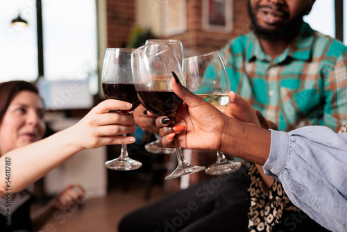 Multiethnic group people hands closeup shot toasting, clinking wine glasses at apartment party. Various nationalities friends celebrating, enjoying together at house gathering.