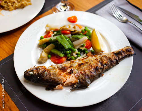 Delicious grilled trout with a slice of lemon and stewed vegetables