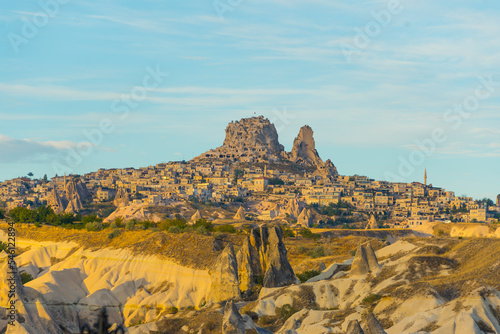 Buildings carved into rocky mountain in Cappadocia, Turkey. Rocky hills and grasslands with clear blue sky and bright yellow summer morning sunlight. Tourist destination. Horizontal shot. High quality
