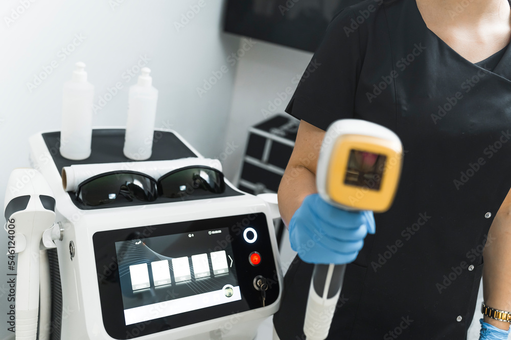  Professional equipment for laser treatment that reduces hair growth in various body areas. Salon laser machine next to unrecognizable caucasian beautician. High quality photo
