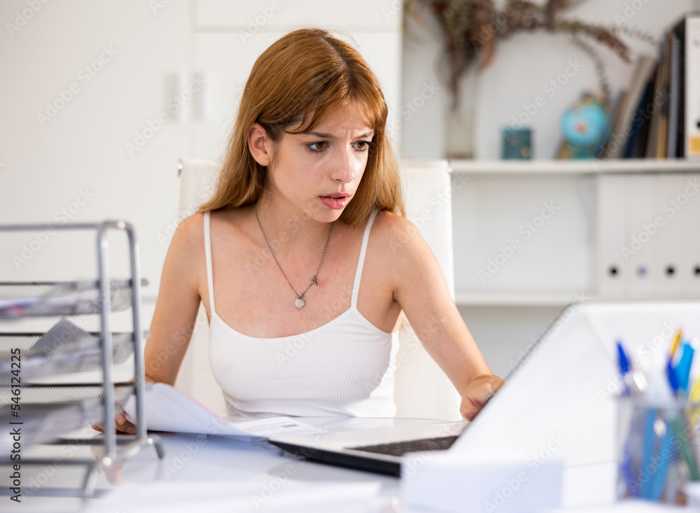 Portrait of woman accountant sitting at table in office and working, using laptop.