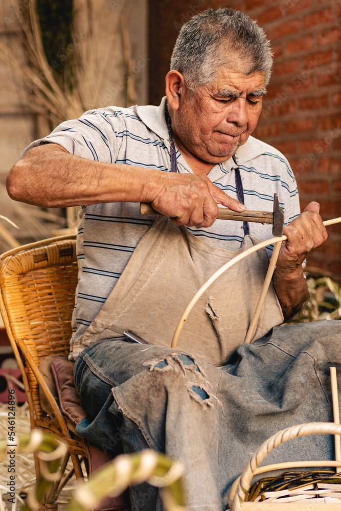 Fototapeta premium Old man using hammer for making wicker baskets at his workshop