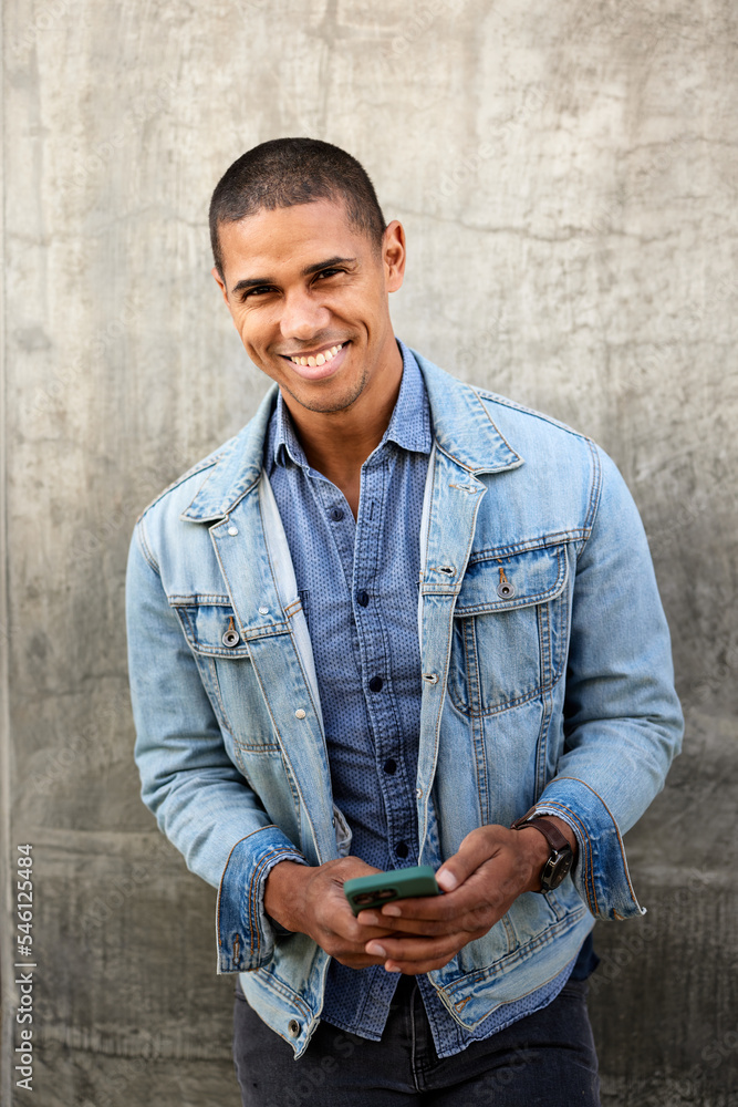 Portrait of smiling man with smart phone standing against wall Portrait of smiling man with smart phone standing against wall