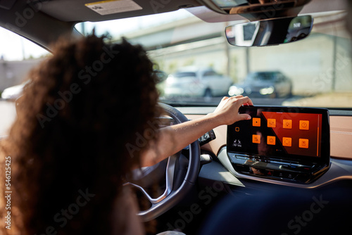 Young woman touching screen of media player sitting in electric car photo