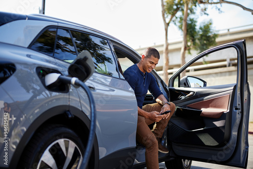Man using smart phone sitting in car getting charged at station