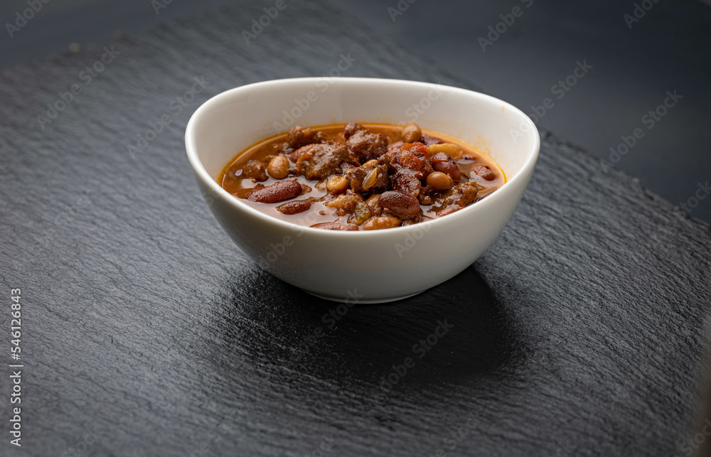 Bowl of chili on black stone background. Pinto beans, peppers, ground meat, onions and spices cooked in slow cooker. Bowl of chili on black stone background. Pinto beans, peppers, ground meat, onions and spices cooked in slow cooker.