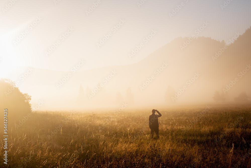Man standing in a misty field looking to the future. Autumn morning and sunshine on a misty field.