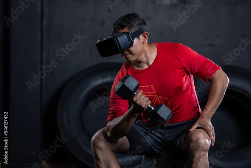 Mexican sportsman doing a weight training exercise by using dumbbell and virtual reality vr goggles, metaverse workout