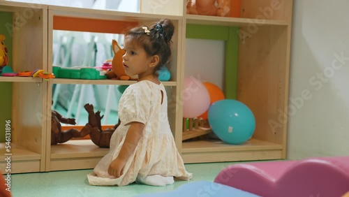 full shot of a little pretty girl sitting on the floor and playing with toys on shelves, kindergarten concept. High quality 4k footage photo