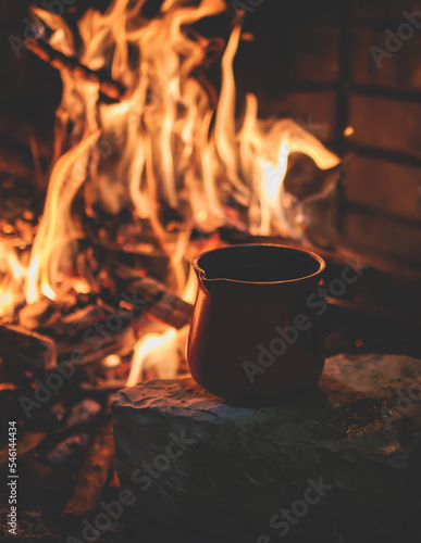 Warming up the fire, cozy winter night in the scandinavian cottage house cabin by the fireplace, burning fire with charcoal and firewood, heating up the drink beverage in the coffee pot