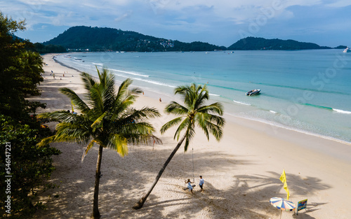 A couple of men and women are on a swing under a palm tree at the beach of Patong Phuket Thailand. Thai women and caucasian men on the ebach photo