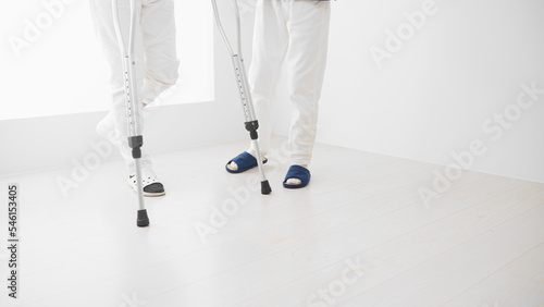 医者に介助されながら松葉杖をついて歩くミドル男性　リハビリイメージ