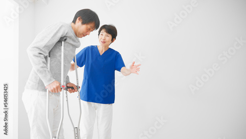 医者に介助されながら松葉杖をついて歩くミドル男性 リハビリイメージ