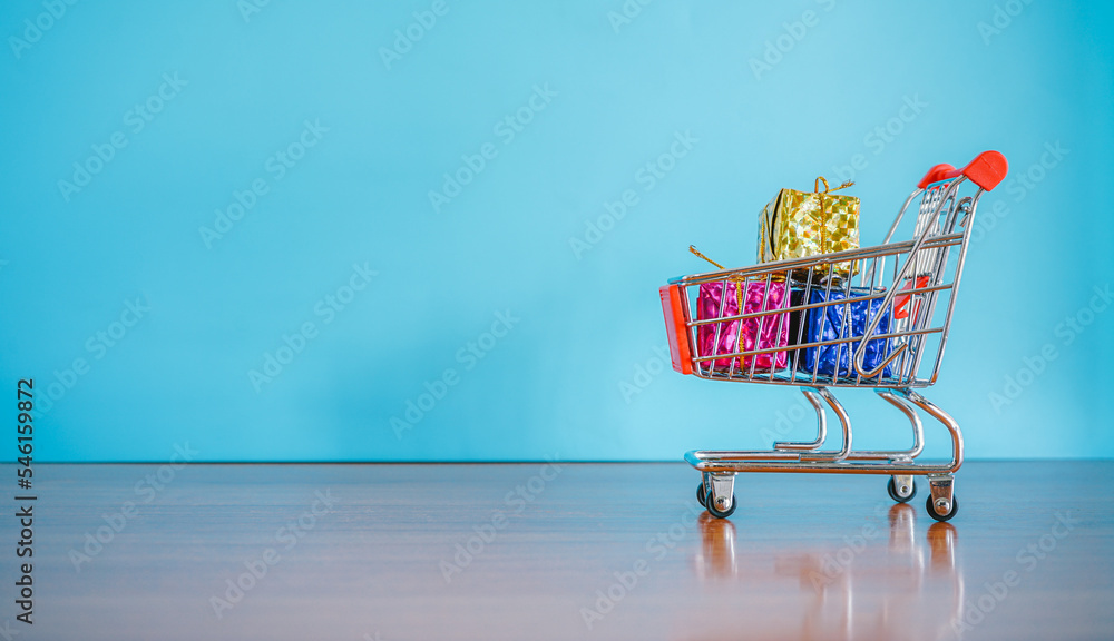 Small shopping cart and gift box on blue background with copy space 