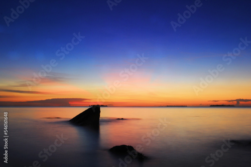 the view of the evening sky colored in gradations of dark blue and orange at the end of the beach with a rock silhouette