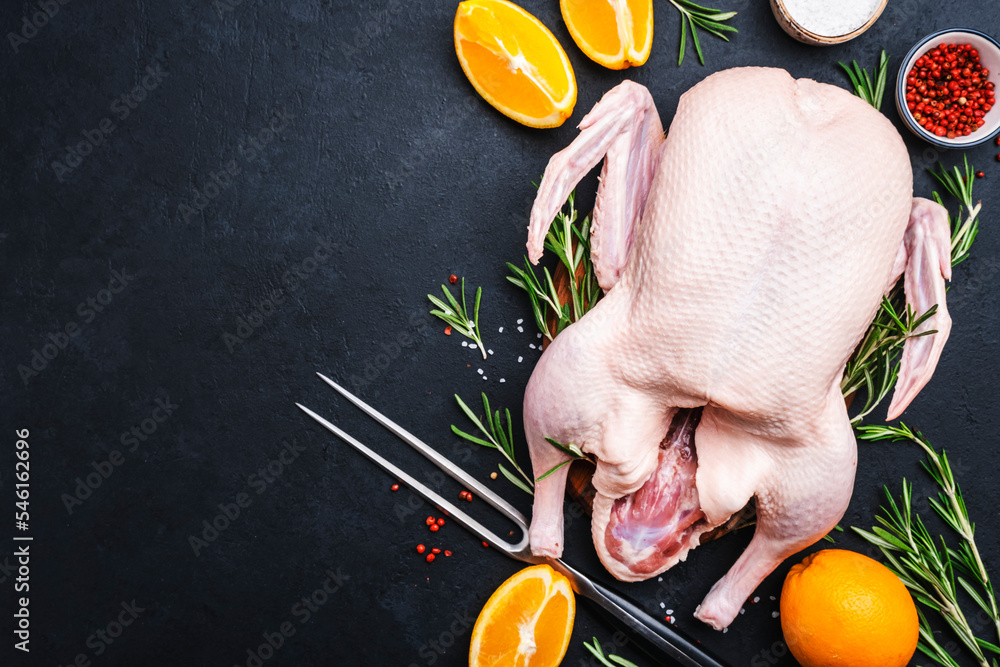 Raw whole duck with orange, pepper and rosemary. Ready to bake for a festive dinner. Black table background. Top view. Copy space - obrazy, fototapety, plakaty 