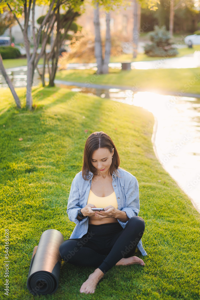 Woman using smartphone, relax after morning workout in the summer park, exercising outdoors. Training workout. Fitness woman. Healthy lifestyle, sport. Beauty Woman using smartphone, relax after morning workout in the summer park, exercising outdoors. Training workout. Fitness woman. Healthy lifestyle, sport. Beauty