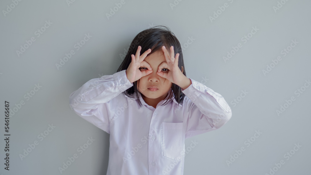 child seriously doing funny faces making with finger glasses shape like glasses looking through binoculars. isolated on light grey background. child seriously doing funny faces making with finger glasses shape like glasses looking through binoculars. isolated on light grey background.