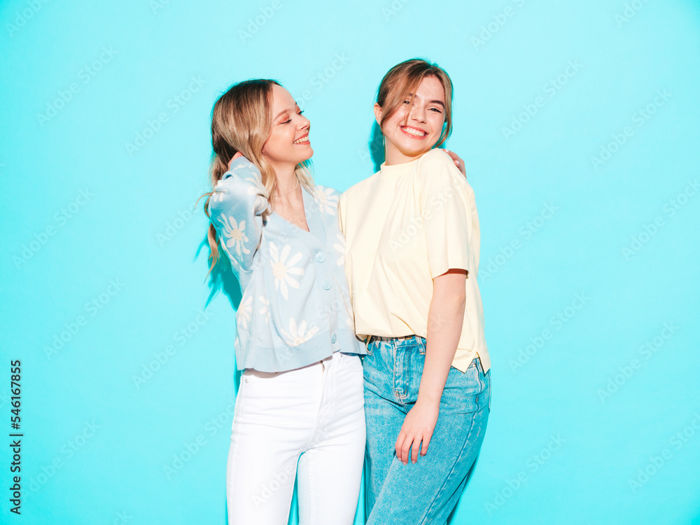 Two young beautiful smiling brunette hipster female in trendy summer clothes. Sexy carefree women posing near blue wall. Positive models having fun. Cheerful and happy Two young beautiful smiling brunette hipster female in trendy summer clothes. Sexy carefree women posing near blue wall. Positive models having fun. Cheerful and happy