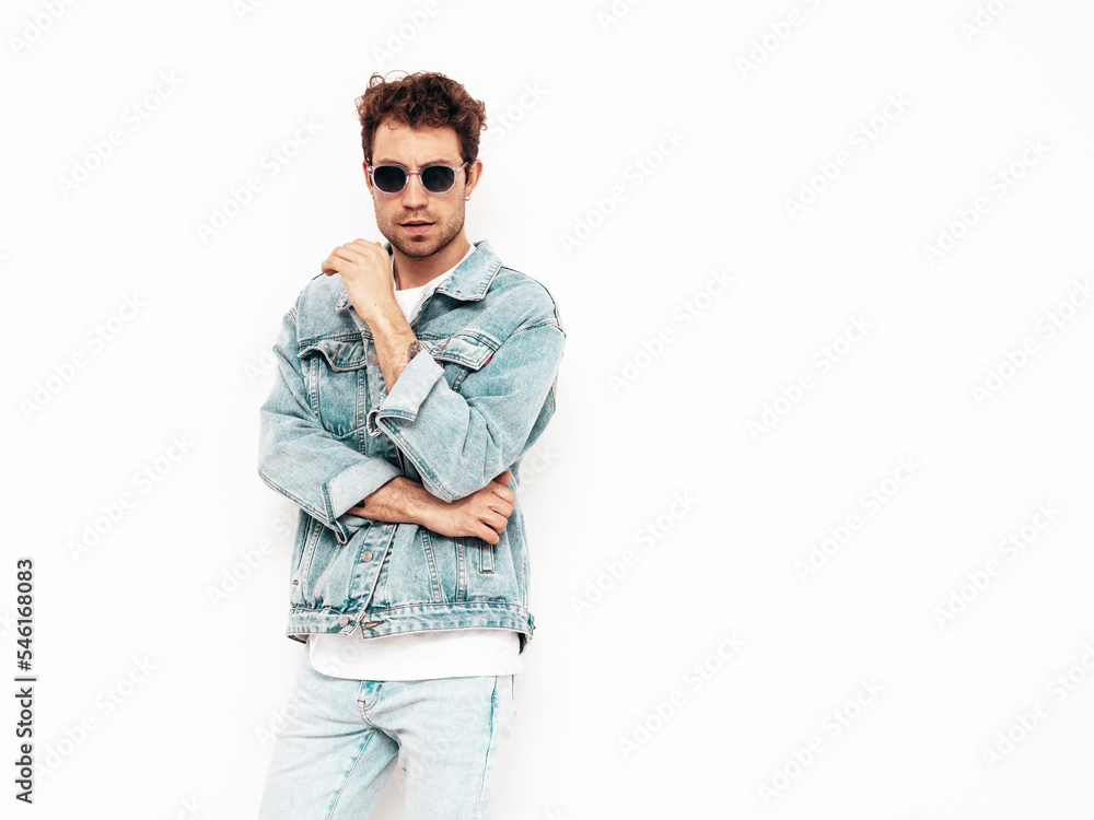 Portrait of handsome confident stylish hipster lambersexual model with curly hairstyle. Sexy man dressed in jeans jacket. Fashion male isolated on white wall in studio Portrait of handsome confident stylish hipster lambersexual model with curly hairstyle. Sexy man dressed in jeans jacket. Fashion male isolated on white wall in studio