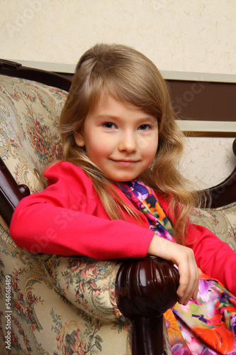 Portrait of a little girl sitting on the couch. A girl in red clothes looks into the camera.