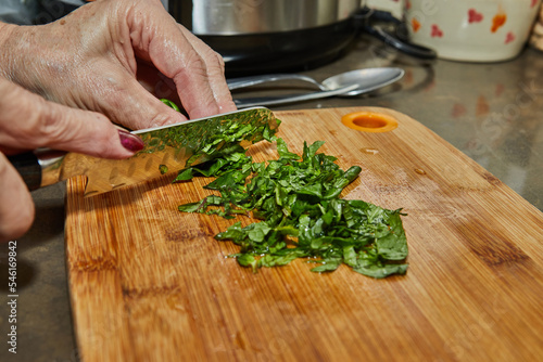 Chef cuts fresh basil leaves on a wooden board for cooking