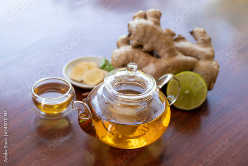 a cup of tea with ginger root, lime, cinnamon and teapot on wooden background. Health drink concept.