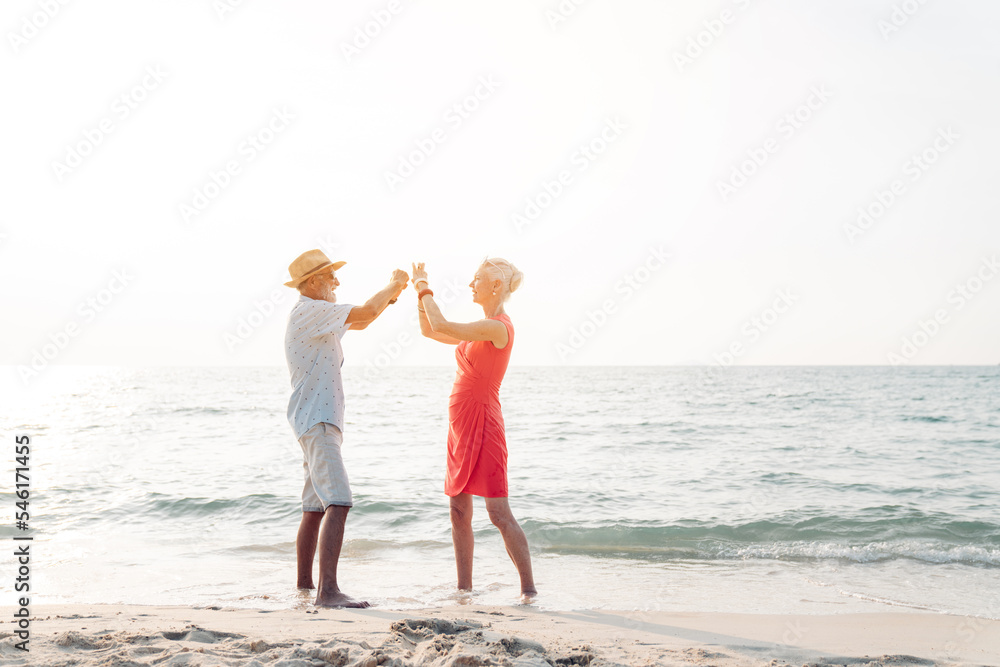 Happy senior couple in love walking and dancing together on the beach having fun in a sunny day, activity after retirement in vacations and summer.